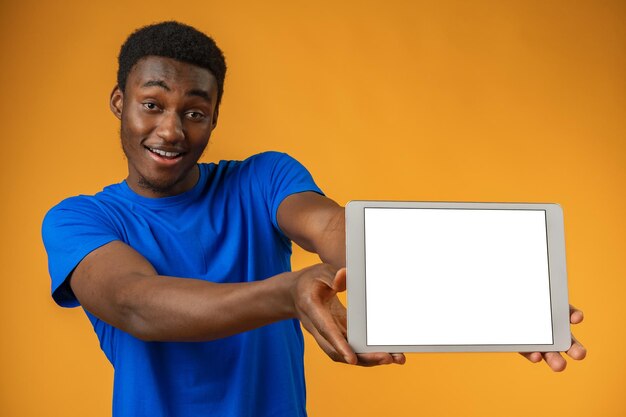 Homem afro-americano mostrando a tela do tablet digital em branco com espaço de cópia no estúdio amarelo