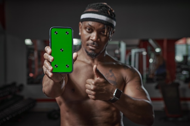 Homem afro-americano mostrando telefone com tela verde com pontos de rastreamento, aplicativo de treino de ginástica e esportes para