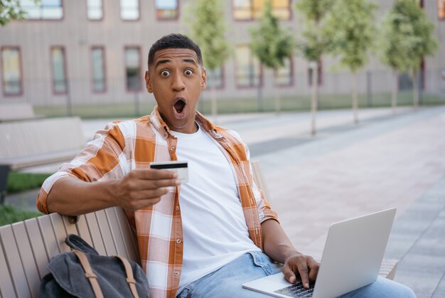 Homem afro-americano muito feliz com compras on-line com cartão de crédito e grandes vendas na Black Friday