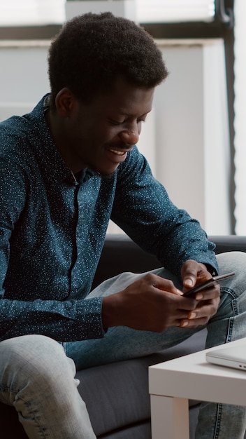 Homem afro-americano negro autêntico positivo sorrindo ao usar um smartphone