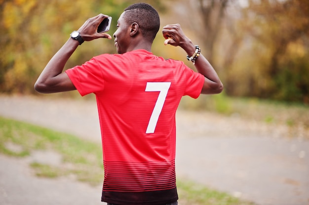 Homem afro-americano no futebol vermelho esporte t-shirt com número 7 contra parque outono.
