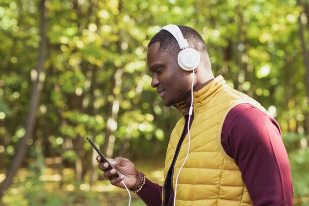 Homem afro-americano ouve música no aplicativo de gadget do parque da primavera e no conceito de serviço de streaming