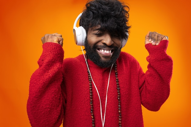 Homem afro-americano ouvindo música com alegria em uma superfície laranja