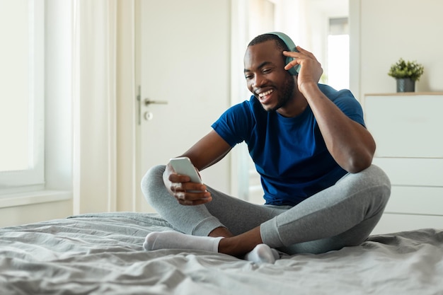 Homem afro-americano ouvindo música usando fones de ouvido no quarto