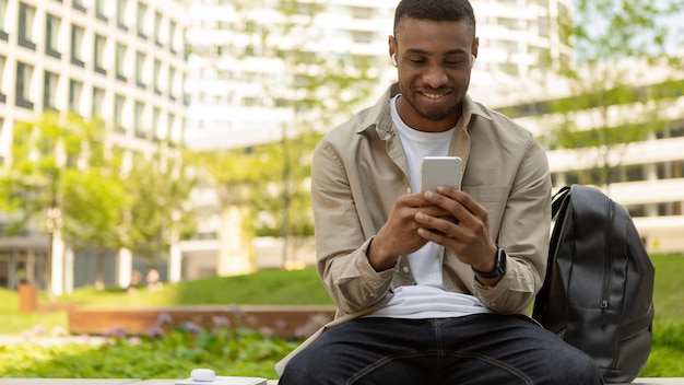 Homem afro-americano ouvindo uma música em fones de ouvido e com um celular na rua