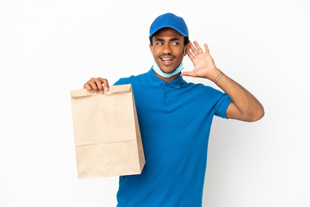 Foto homem afro-americano pegando uma sacola de comida para viagem isolada no fundo branco, ouvindo algo colocando a mão na orelha