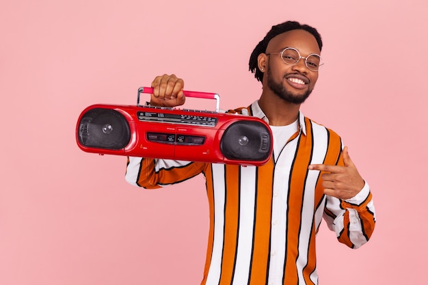 Homem afro-americano positivo apontando o dedo para uma vitrola de áudio vintage vermelha, curtindo a música