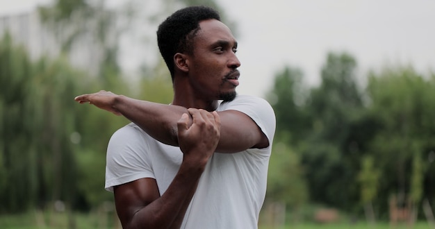 Homem afro-americano se aquecendo e se alongando no parque ao ar livre para se exercitar