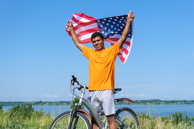 Homem afro-americano segurando e acenando a bandeira dos eua em pé com uma bicicleta