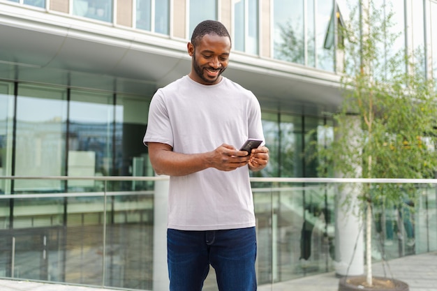 homem afro-americano segurando um smartphone com tela sensível ao toque digitando página de rolagem em uma rua urbana na cidade cara