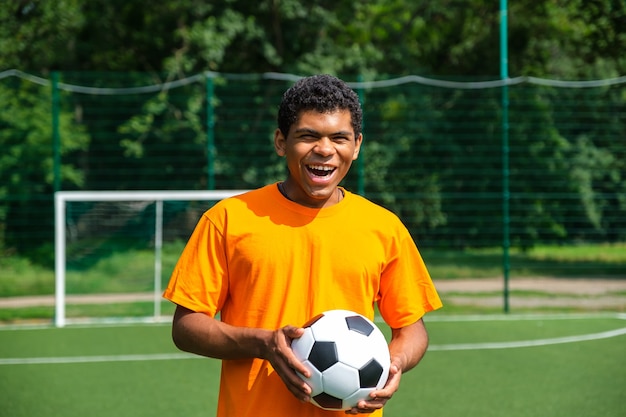 Homem afro-americano segurando uma bola de futebol em uma quadra de esportes