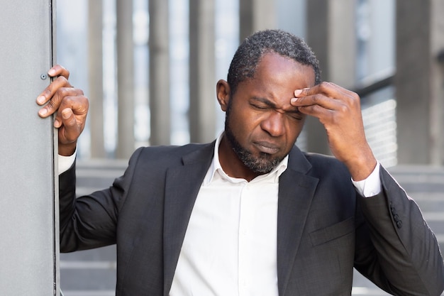 Homem afro-americano sênior sofrendo de forte pressão de dor de cabeça, ele está do lado de fora do