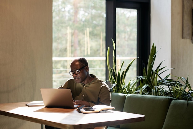 Homem afro-americano sênior trabalhando no laptop enquanto está sentado à mesa no café