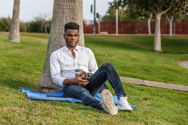 Homem afro-americano sentado debaixo de uma árvore usando um telefone celular