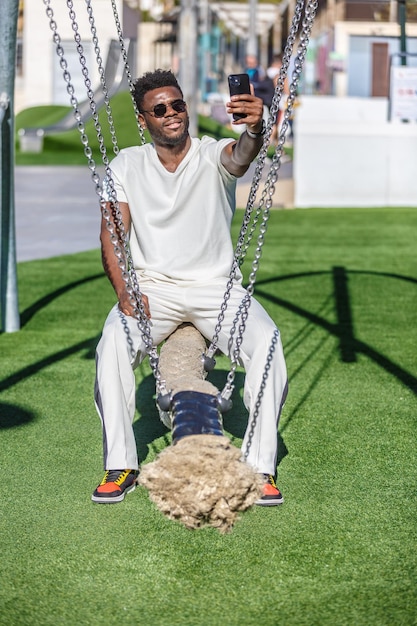 Homem afro-americano sentado em um swing segurando um telefone celular em um parque público