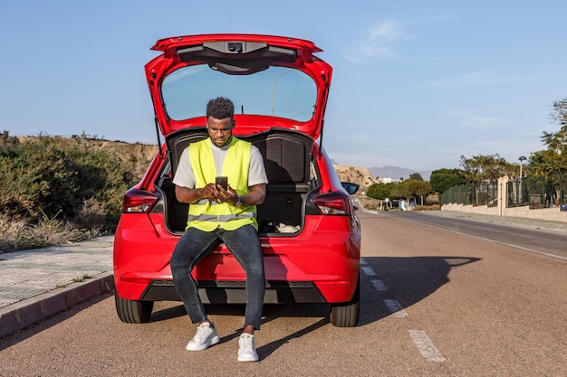 Homem afro-americano sentado na parte de trás de um carro vermelho usando um telefone celular