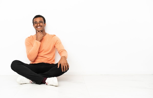 Homem afro-americano sentado no chão sobre um fundo isolado copyspace com óculos e sorrindo