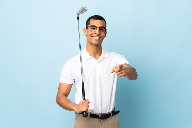 Homem afro-americano sobre fundo azul isolado jogando golfe e apontando para a frente