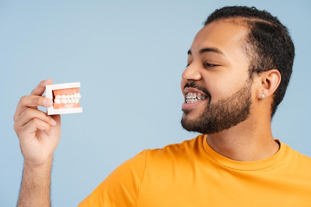 Homem afro-americano sorridente com aparelho dentário olhando para o molde dental com aparelho dental