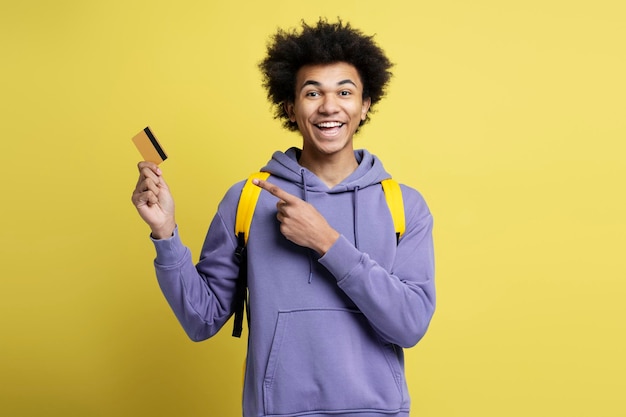 Homem afro-americano sorridente segurando o cartão de crédito isolado em fundo amarelo. compras, vendas