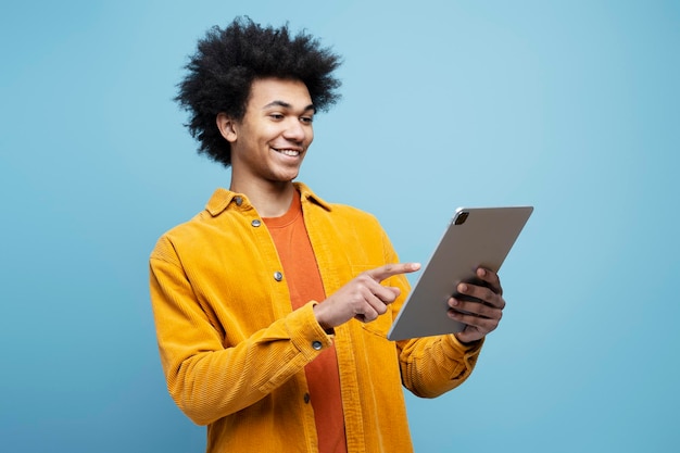 Homem afro-americano sorridente segurando tablet digital assistindo vídeos isolados em fundo azul