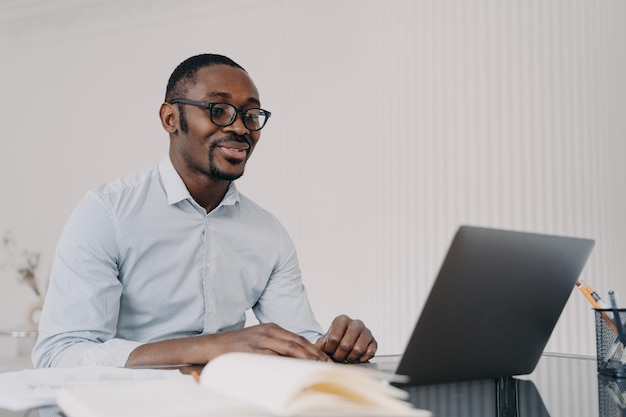 Homem afro-americano sorridente trabalhando em laptop em projeto de negócios lendo e-mail com boas notícias