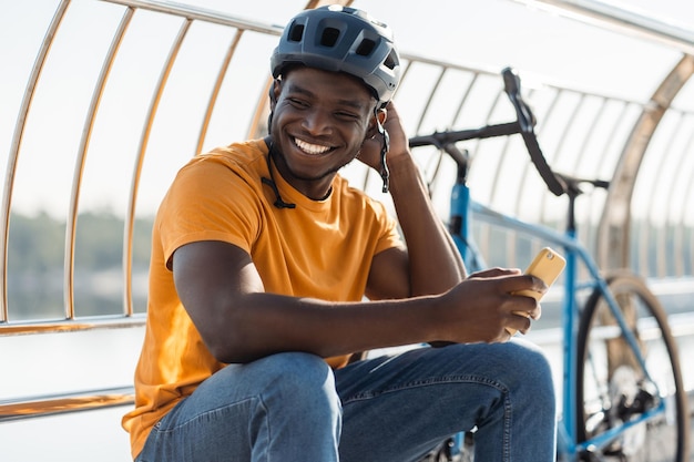 homem afro-americano sorridente usando capacete protetor segurando telefone móvel comunicação online