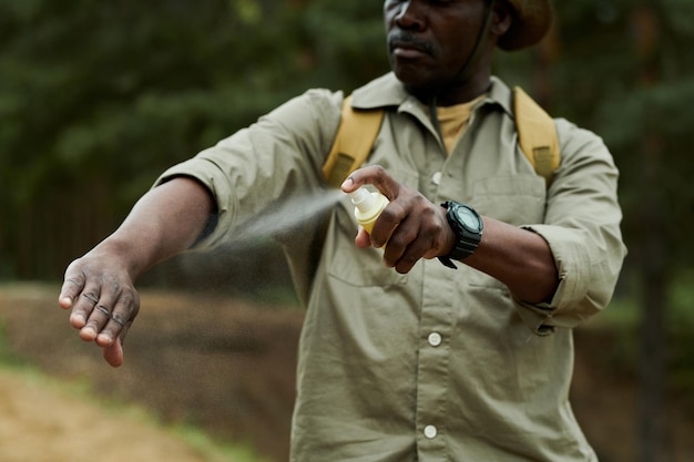 Homem afro-americano usando spray de mosquito durante caminhadas