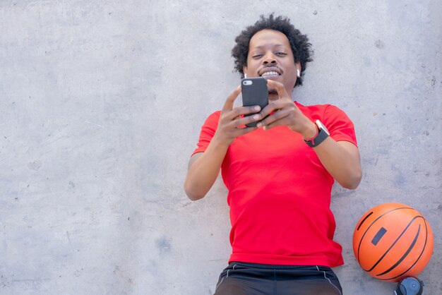 Homem afro-atlético usando seu telefone celular e relaxando depois do treino ao ar livre.