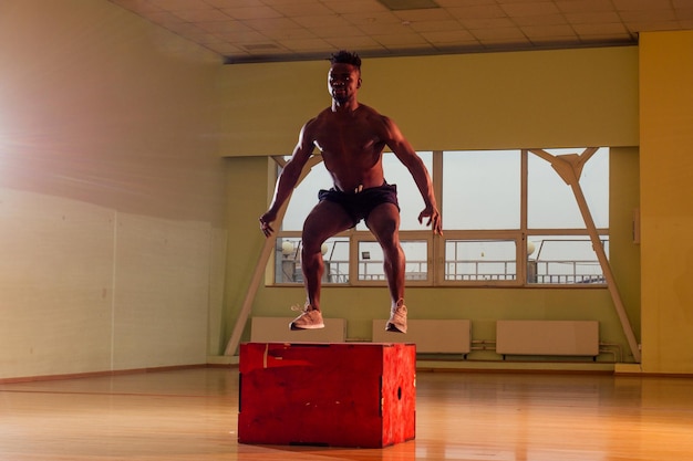 Homem afro fazendo exercício com uma caixa de ajuste em uma academia.