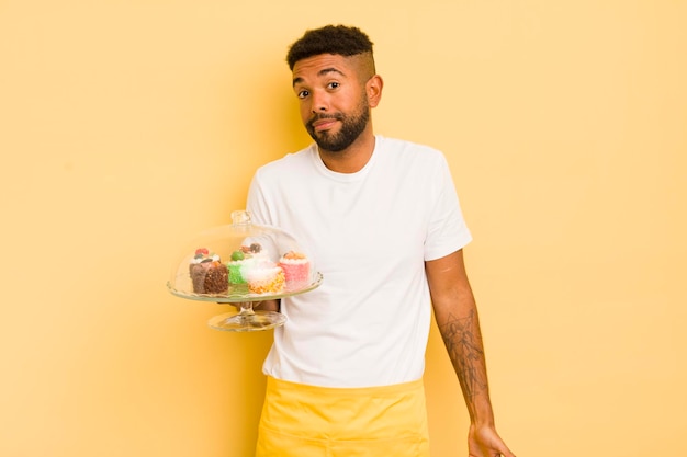 Homem afro negro encolhendo os ombros sentindo-se confuso e incerto conceito de bolos caseiros