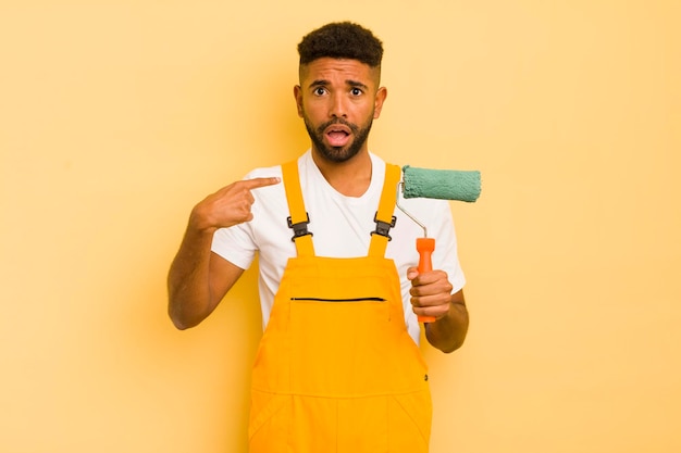 Foto homem afro negro parecendo chocado e surpreso com a boca aberta apontando para o conceito de casa autopintada