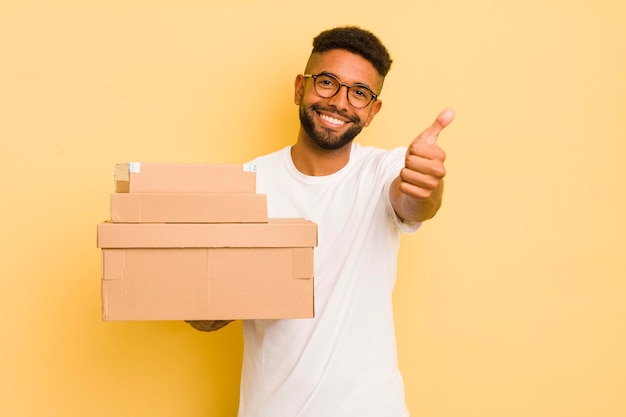 Homem afro negro se sentindo orgulhoso sorrindo positivamente com polegares para cima conceito de caixas de transporte