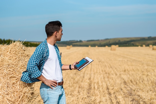 Homem agricultor de jeans e uma camisa com um tablet nas mãos está no campo