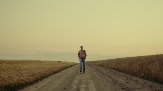 Homem agrônomo de pequenas empresas cruzando a paisagem do pôr do sol com campo dourado sozinho