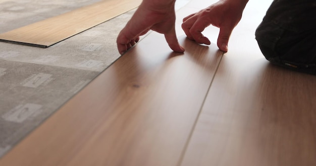 Homem ajoelhado e instalando piso laminado de madeira em uma casa Closeup em mãos masculinas