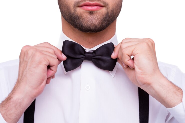 Foto homem ajustando a gravata borboleta. close-up de jovem em camisa branca ajustando a gravata borboleta em pé, isolado no branco