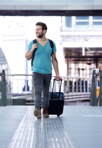 Homem alegre, andando com malas na estação de trem