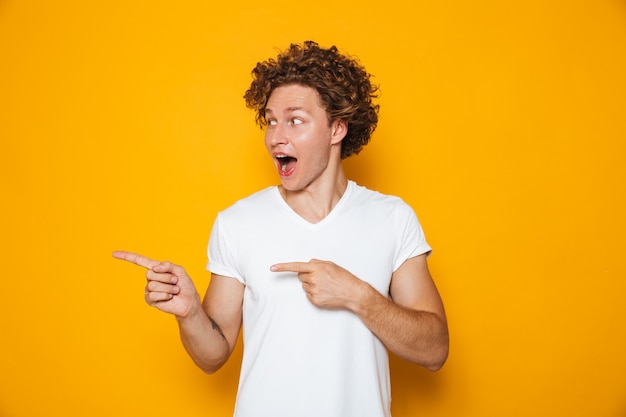 Homem alegre animado com cabelo castanho encaracolado, gesticulando o dedo de lado na copyspace