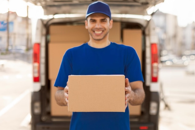 Homem alegre carregando um pacote de um carro de entrega segurando uma caixa de papelão e um serviço de correio sorridente