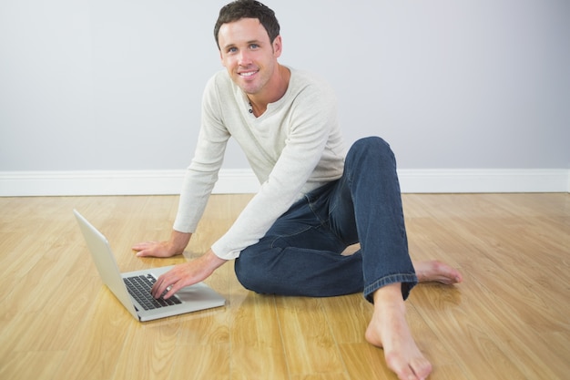 Homem alegre casual sentado no chão usando o laptop