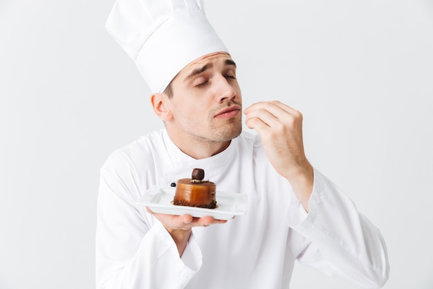 Homem alegre chef cozinheiro vestindo uniforme mostrando massa em um prato isolado sobre uma parede branca