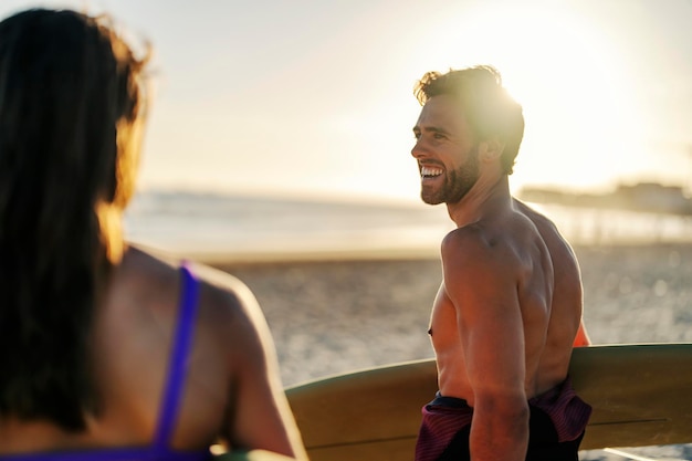Homem alegre com prancha de surf está conversando com seu amigo enquanto caminhava na praia