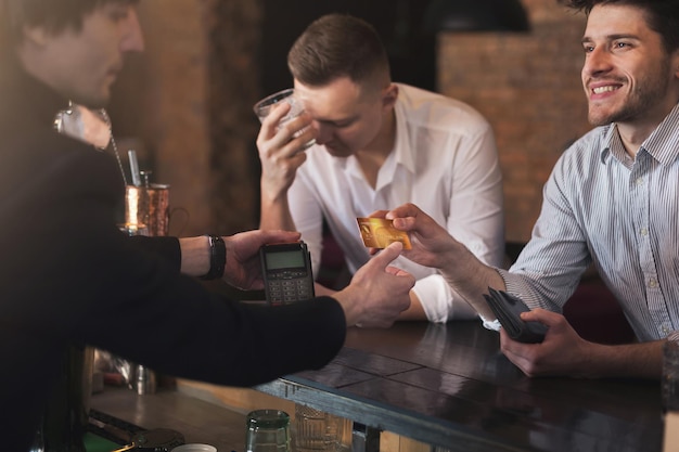 Homem alegre dando cartão de crédito para barman no bar, pagamento sem dinheiro para bebida, espaço de cópia