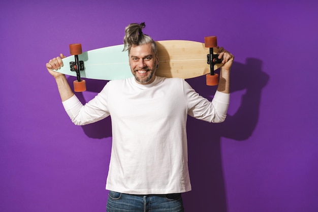 Homem alegre de meia-idade com longboard vestindo camisola branca contra fundo roxo