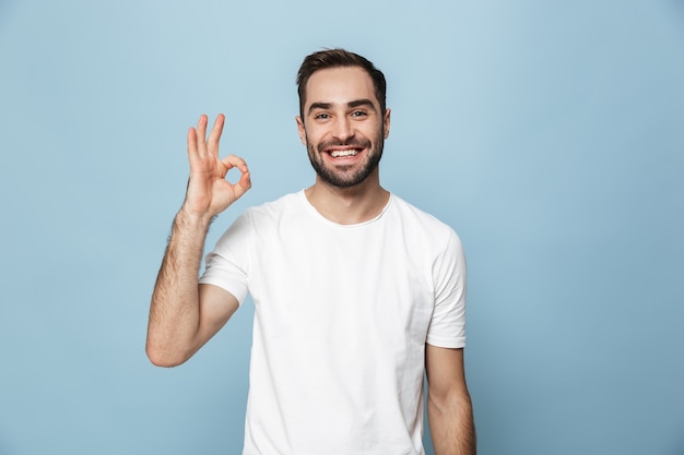 Homem alegre e animado vestindo uma camiseta em branco, isolado na parede azul, ok