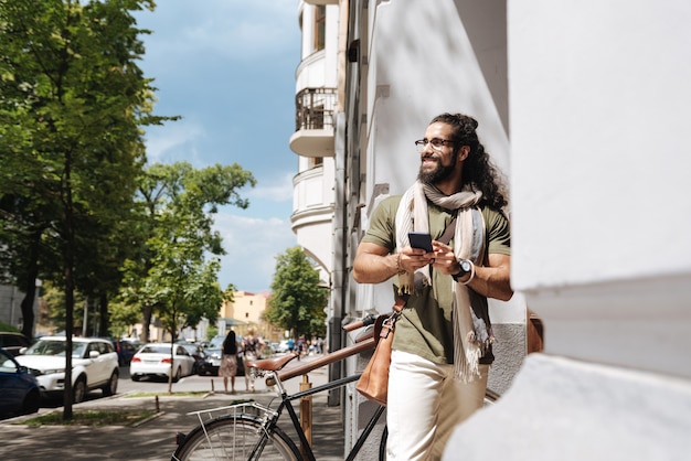 Homem alegre e positivo olhando para a rua em pé com seu smartphone