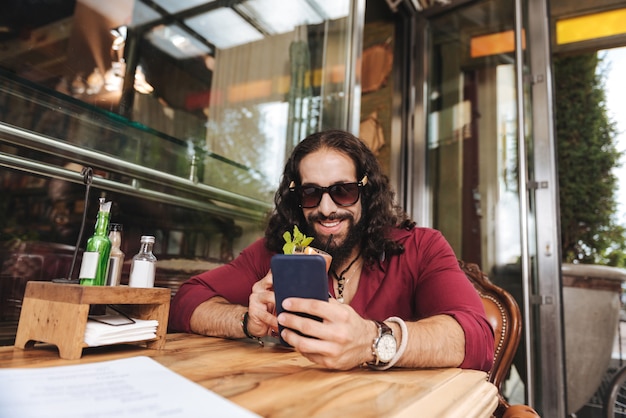 Homem alegre e positivo sorrindo enquanto usa seu dispositivo móvel