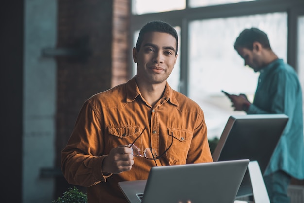 Homem alegre e simpático segurando seus óculos enquanto se distrai do trabalho