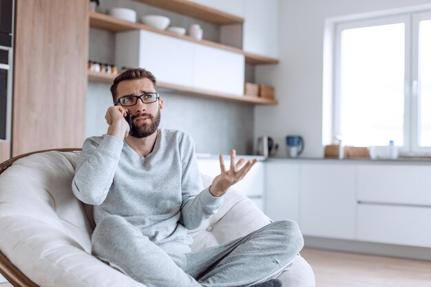 Homem alegre falando em um telefone celular sentado em uma cadeira confortável